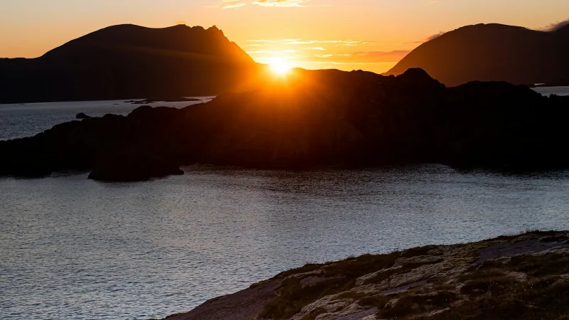 A blue and red tent on rock near water at sunset