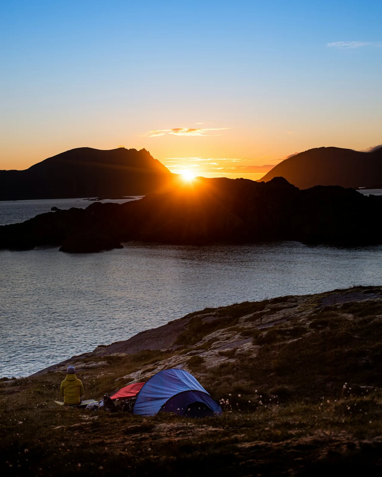 A blue and red tent on rock near water at sunset