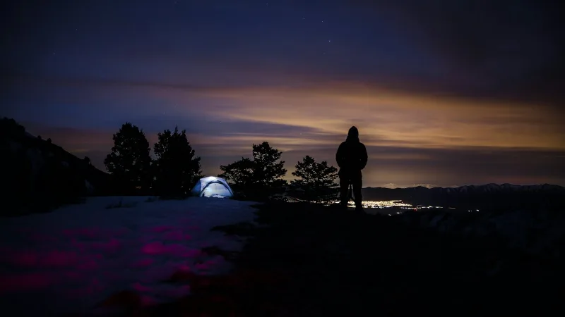 A hooded hiker at night with a tent behind