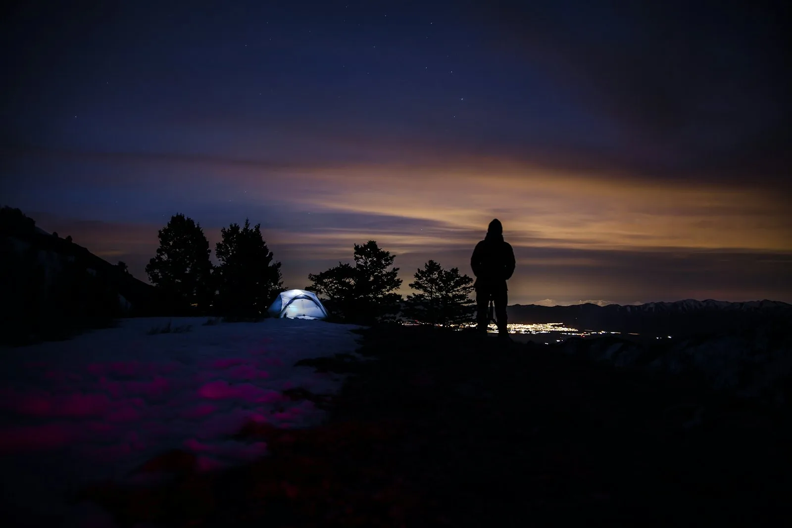 A hooded hiker at night with a tent behind
